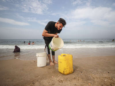 A Palestinian man fills empty bottles with sea water due to water crisis as a result of the suspension of water flow in the water pipes from Israel to the Gaza Strip in Deir al-Balah, Gaza on October 29, 2023.