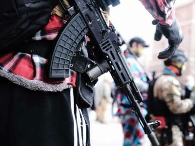 A man carrying an assault rifile stands near other men carrying assault rifles during an outdoor "demonstration"