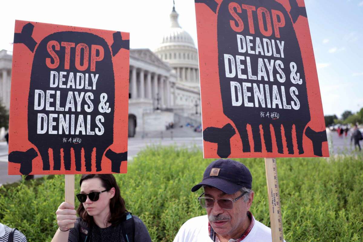 Two people hold signs reading "STOP DEADLY DELAYS AND DENIALS" during an outdoor rally at the U.S. capitol