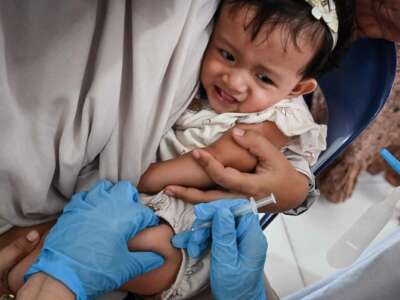 A baby receives a vaccine as she's held by a parent