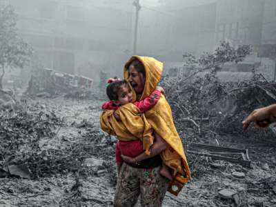 A woman sobs while holding a child amidst the rubble of homes destroyed by Israeli airstikes