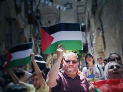 Ofer Cassif holds a poster bearing the Palestinian flag as he participates in an outdoor demonstration