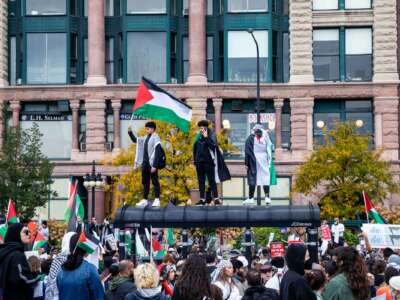 People wave Palestinian flags while standing on top of a bus station during a protest in downtown Chicago