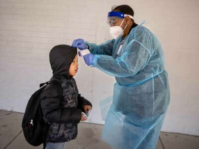 A school nurse in ppe takes a student's temperature