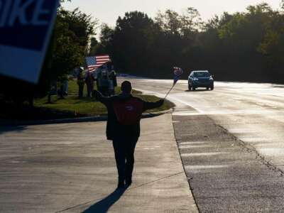 A person holding two small U.S. flags walks towards a group of striking United Auto Workers union members