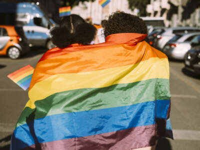 Friends wrapped in rainbow flag on sunny day