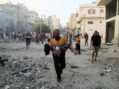 A Palestinian man carrying a child runs following an Israeli strike in Khan Yunis in the southern Gaza Strip, on October 14, 2023.