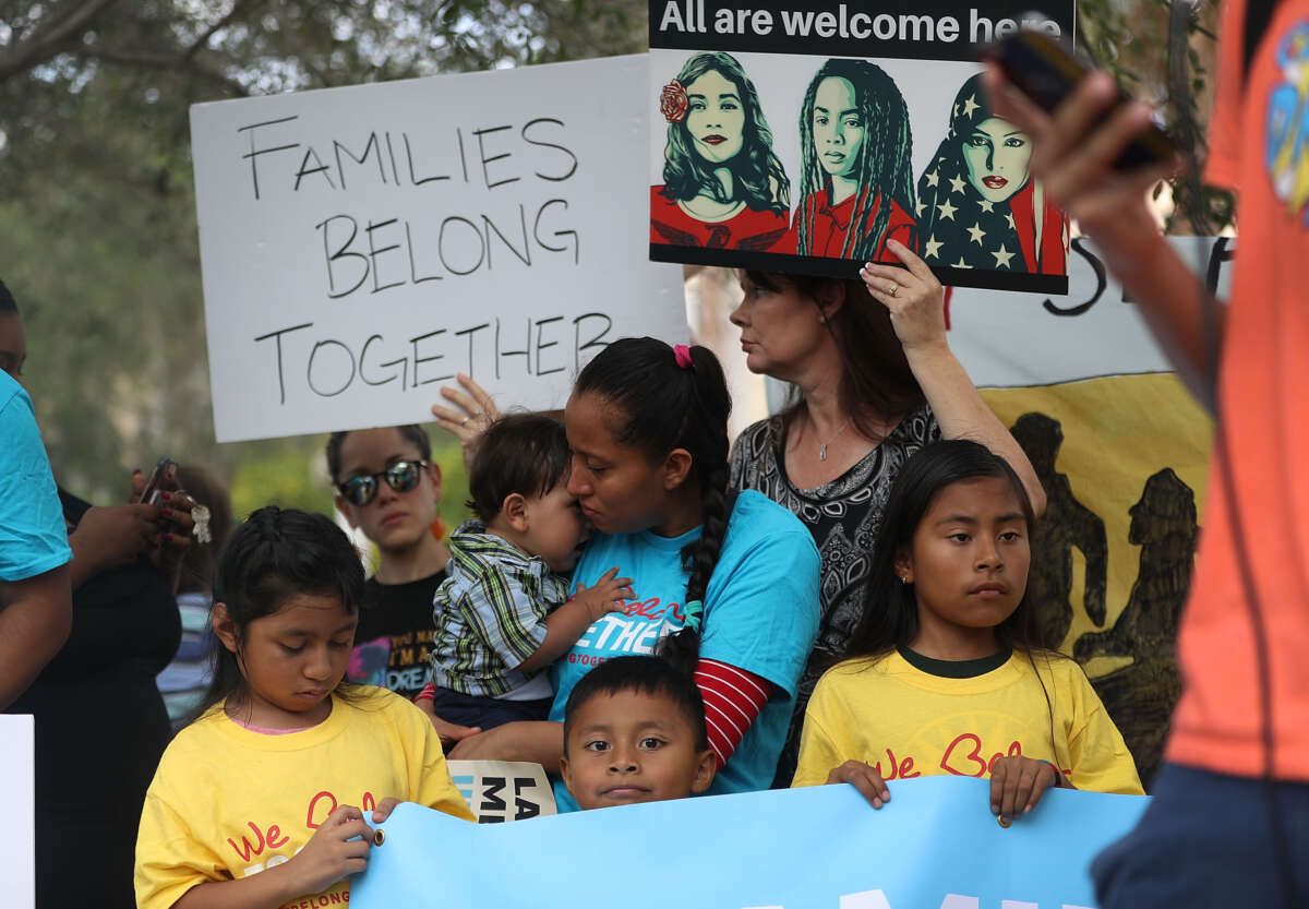 Protesters hold signs that say "families belong together" and "all are welcome here" outside of a migrant prison