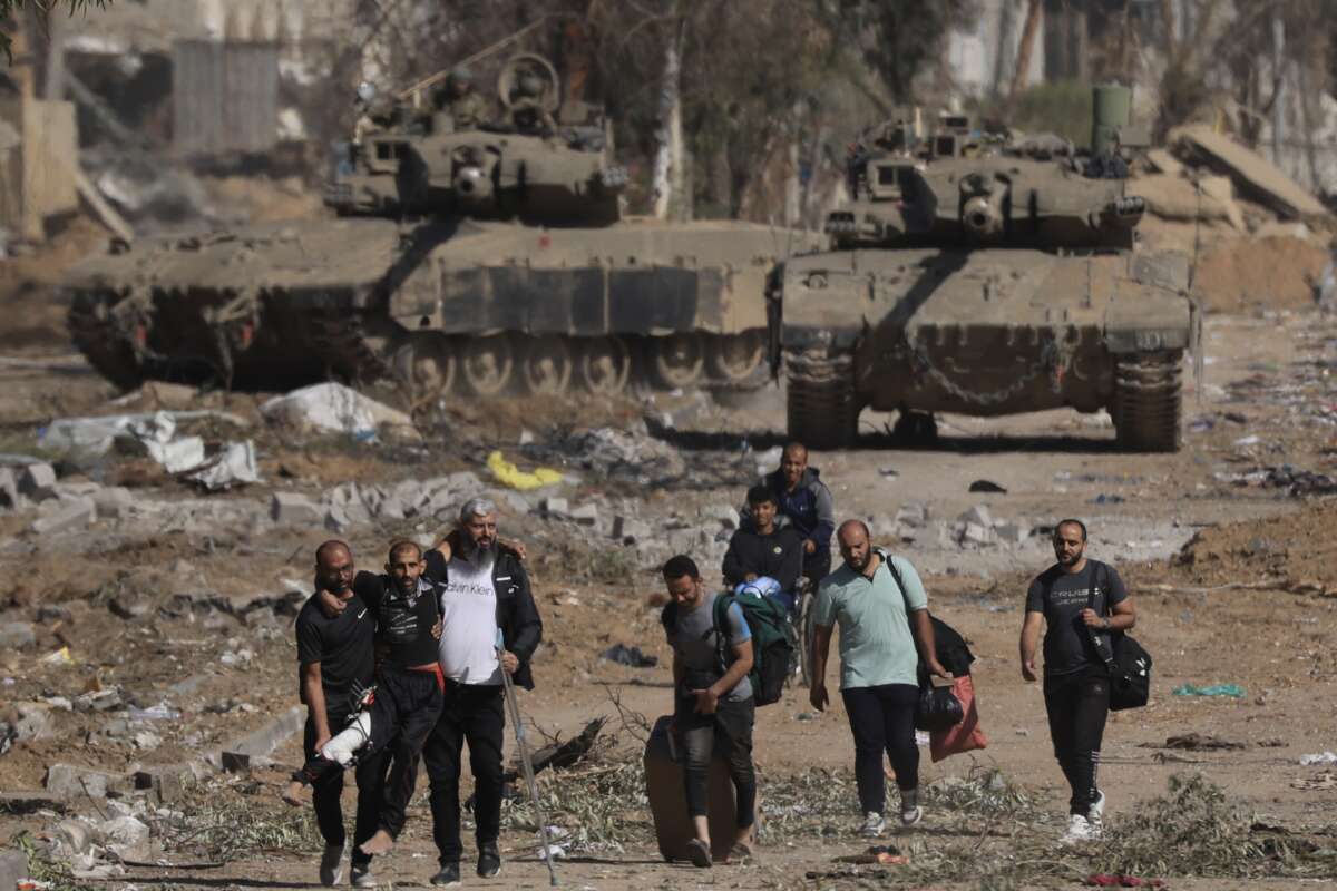 Palestinians fleeing the north along Salaheddine road help a man with a bandaged leg as they walk in front of Israeli army tanks in the Zeitoun district on the southern outskirts of Gaza City on November 24, 2023, following a four-day military pause that began early in the morning.