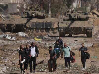 Palestinians fleeing the north along Salaheddine road help a man with a bandaged leg as they walk in front of Israeli army tanks in the Zeitoun district on the southern outskirts of Gaza City on November 24, 2023, following a four-day military pause that began early in the morning.