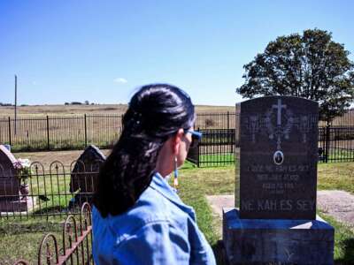 A woman stands in a graveyard, her attention toward the prominently displayed headstone of Lizzie Ne Kah Es Say (1848 - 1921)