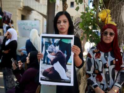 A woman holds a protest sign of a Palestinian mother holding the shrouded body of her deceased child