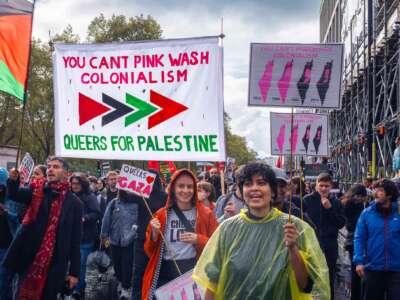 Protesters march under a banner reading "YOU CAN'T PINKWASH COLONIALISM; QUEERS FOR PALESTINE" during an outdoor demonstration