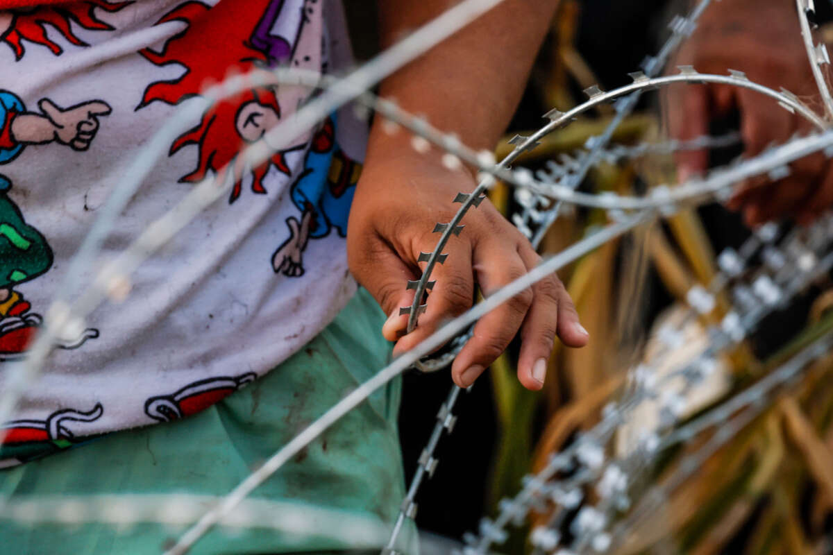 A boy carefully grips razor wire as he emerges from the banks of the Rio Grande after crossing over the U.S. / Mexico border with family, at Eagle Pass, Texas, on September 23, 2023.