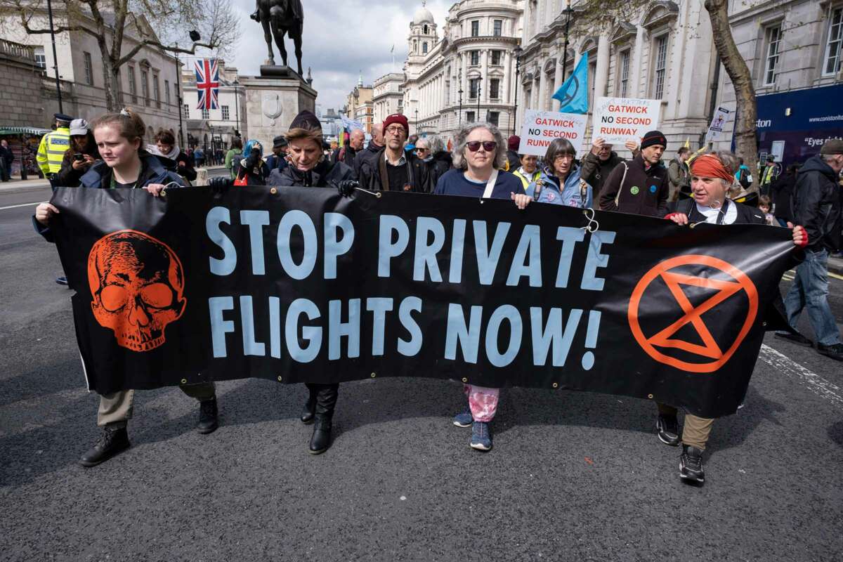 People march behind a banner reading "STOP PRIVATE FLIGHTS NOW" during an outdoor demonstration