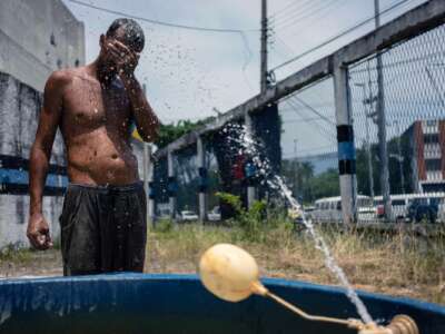 A man covers his face while a makeshift sprinkler sprays him with water