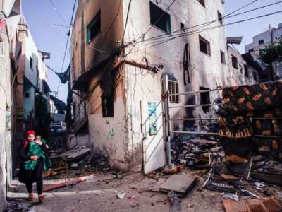 A woman carries a baby through a rubble-strewn street