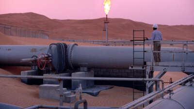 A worker stands at a pipeline, watching a flare stack at the Saudi Aramco oil field complex facilities at Shaybah in the Rub' al Khali desert on March 2003 in Shaybah, Saudi Arabia.