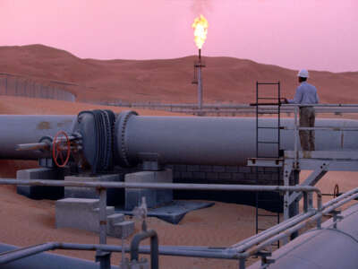 A worker stands at a pipeline, watching a flare stack at the Saudi Aramco oil field complex facilities at Shaybah in the Rub' al Khali desert on March 2003 in Shaybah, Saudi Arabia.