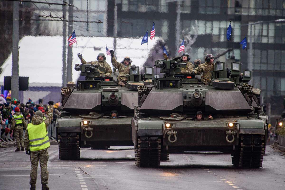 US Army tanks roll down a city street leaving behind a wake of visibly heated air behind them