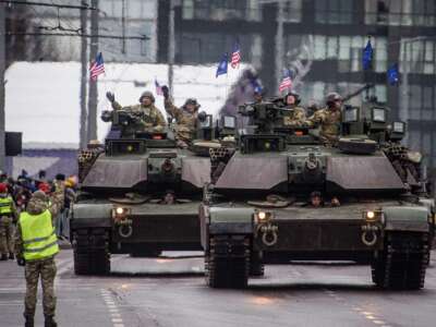 US Army tanks roll down a city street leaving behind a wake of visibly heated air behind them