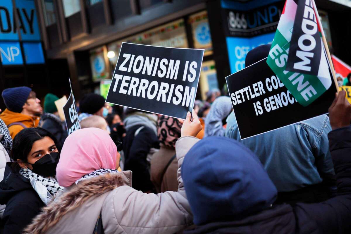 A person holds a sign reading "ZIONISM IS TERRORISM" during an outdoor protest