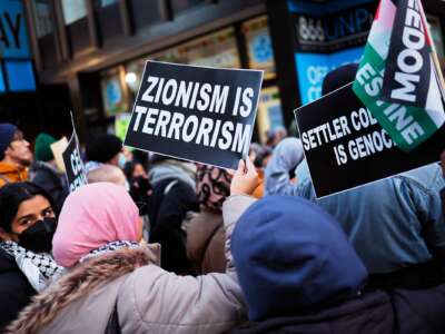 A person holds a sign reading "ZIONISM IS TERRORISM" during an outdoor protest