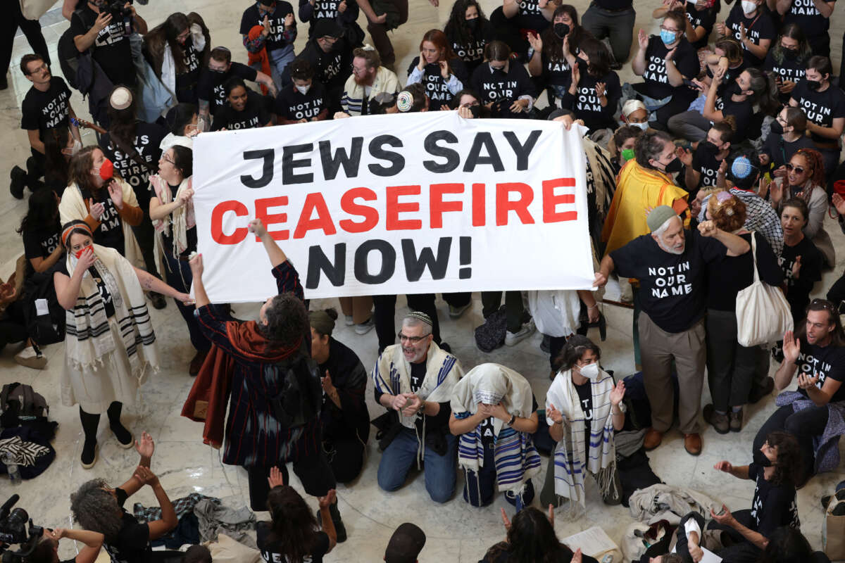 Protesters wearing shirts that say "Not in our name" hold up a sign that says "Jews say ceasefire now" in a congressional office building