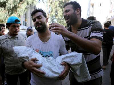 A Palestinian holds the body of a child wrapped in a shroud as another stands next to him, outside a hospital following Israel's bombardment of Gaza City's eastern suburb of Shujaiya, on November 4, 2023.