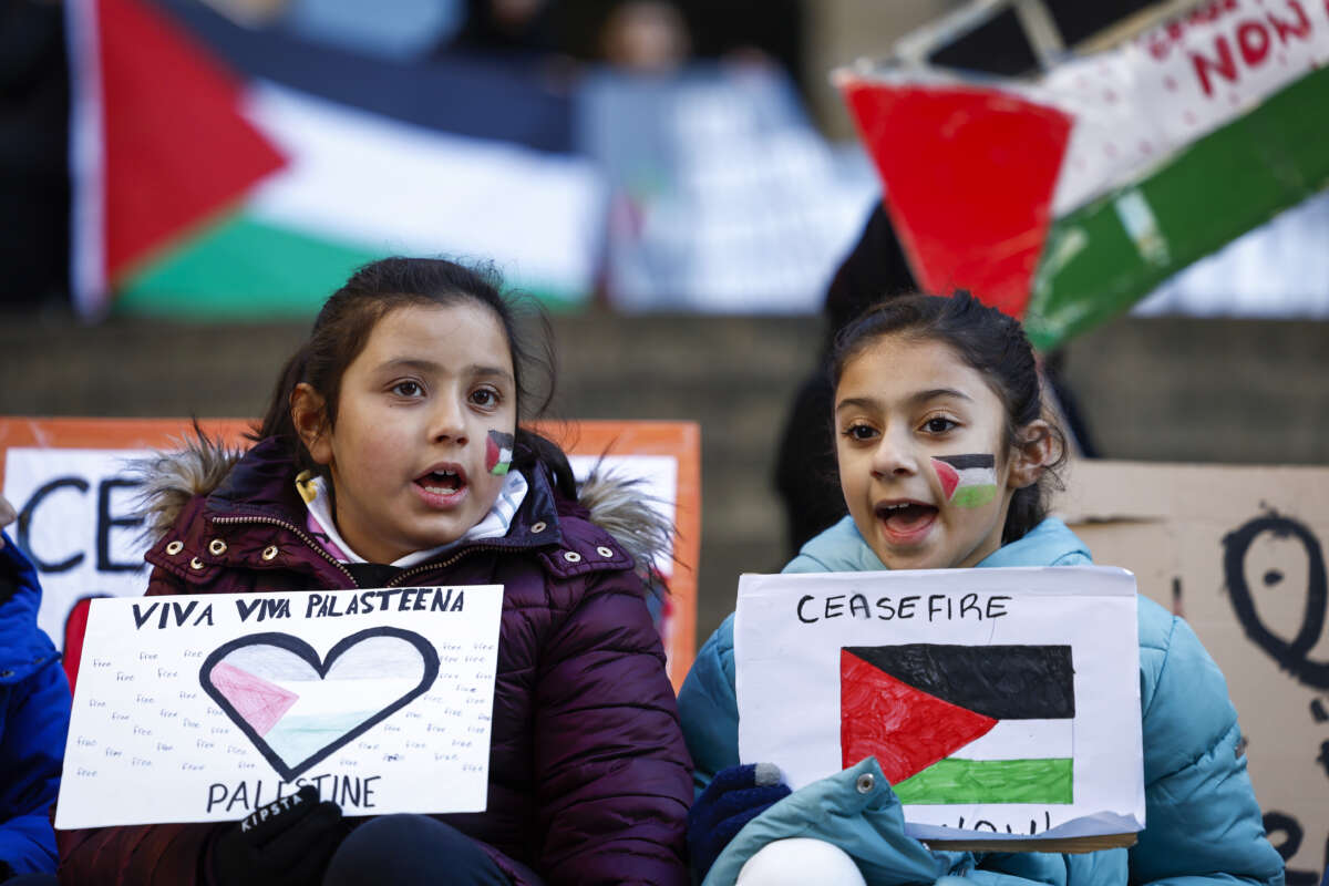 Two elementary-school aged girls hold signs depicting the Palestinian flag at a protest