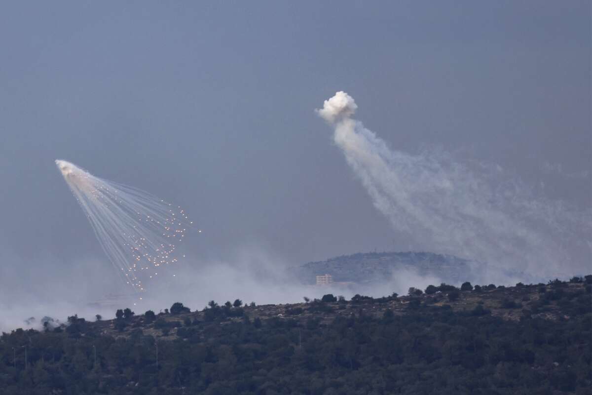 A picture taken from the Israeli side of border with Lebanon shows shells exploding over hills around the southern Lebanese village of Aita al-Shaab on December 8, 2023.