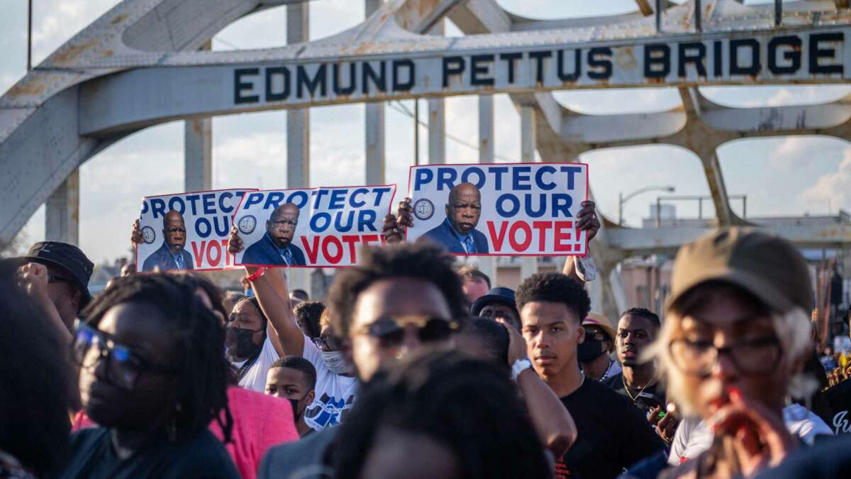 People march across the Edmund Pettus Bridge in Selma, Alabama, holding signs bearing the late Sen. John Lewis's face and the words "PROTECT OUR VOTE"