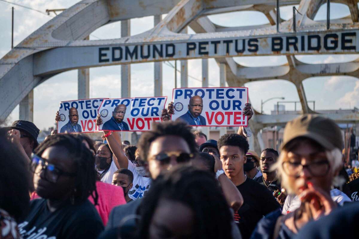 People march across the Edmund Pettus Bridge in Selma, Alabama, holding signs bearing the late Sen. John Lewis's face and the words "PROTECT OUR VOTE"