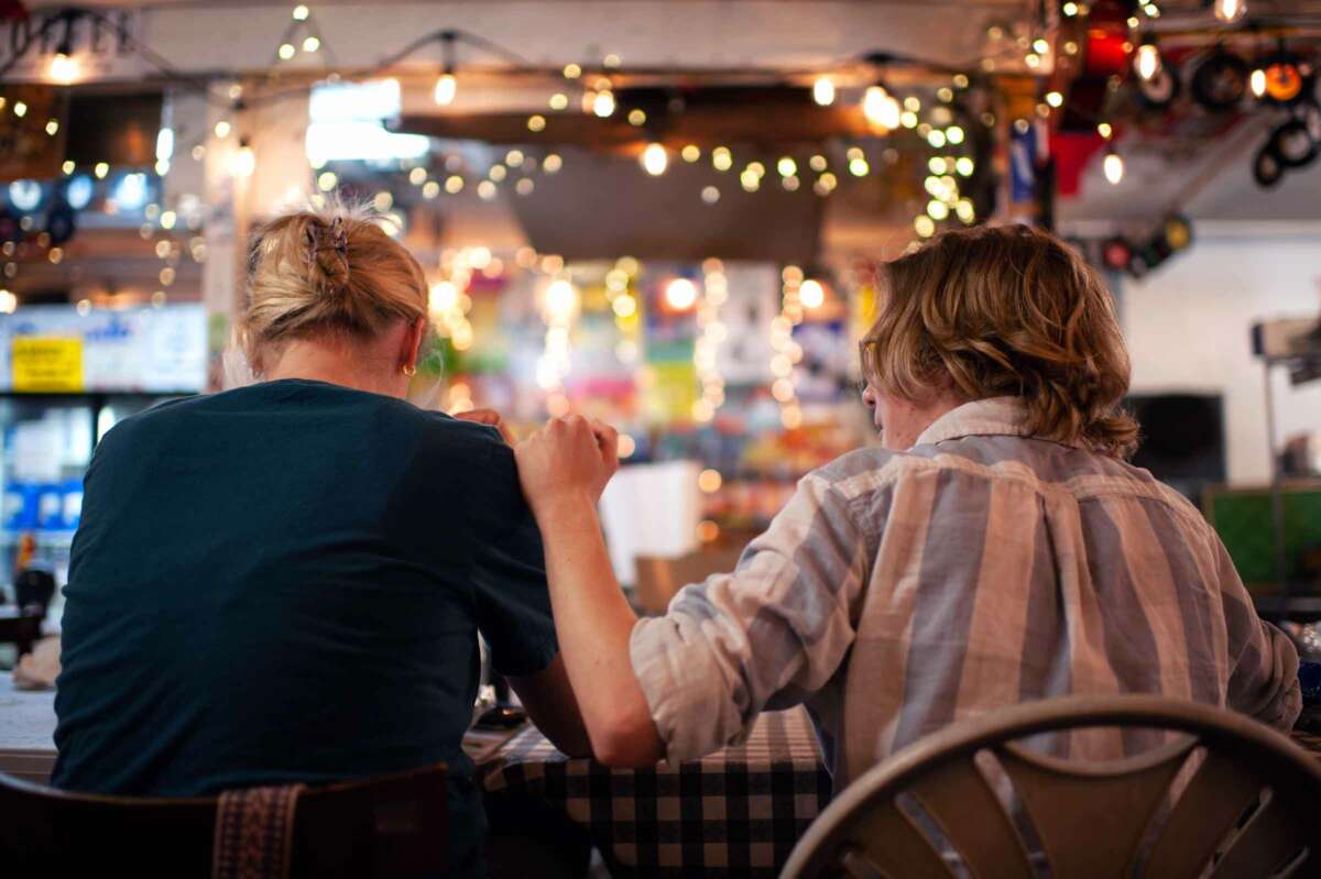 A man in a blue and white plaid shirt comforts a woman sitting to his left