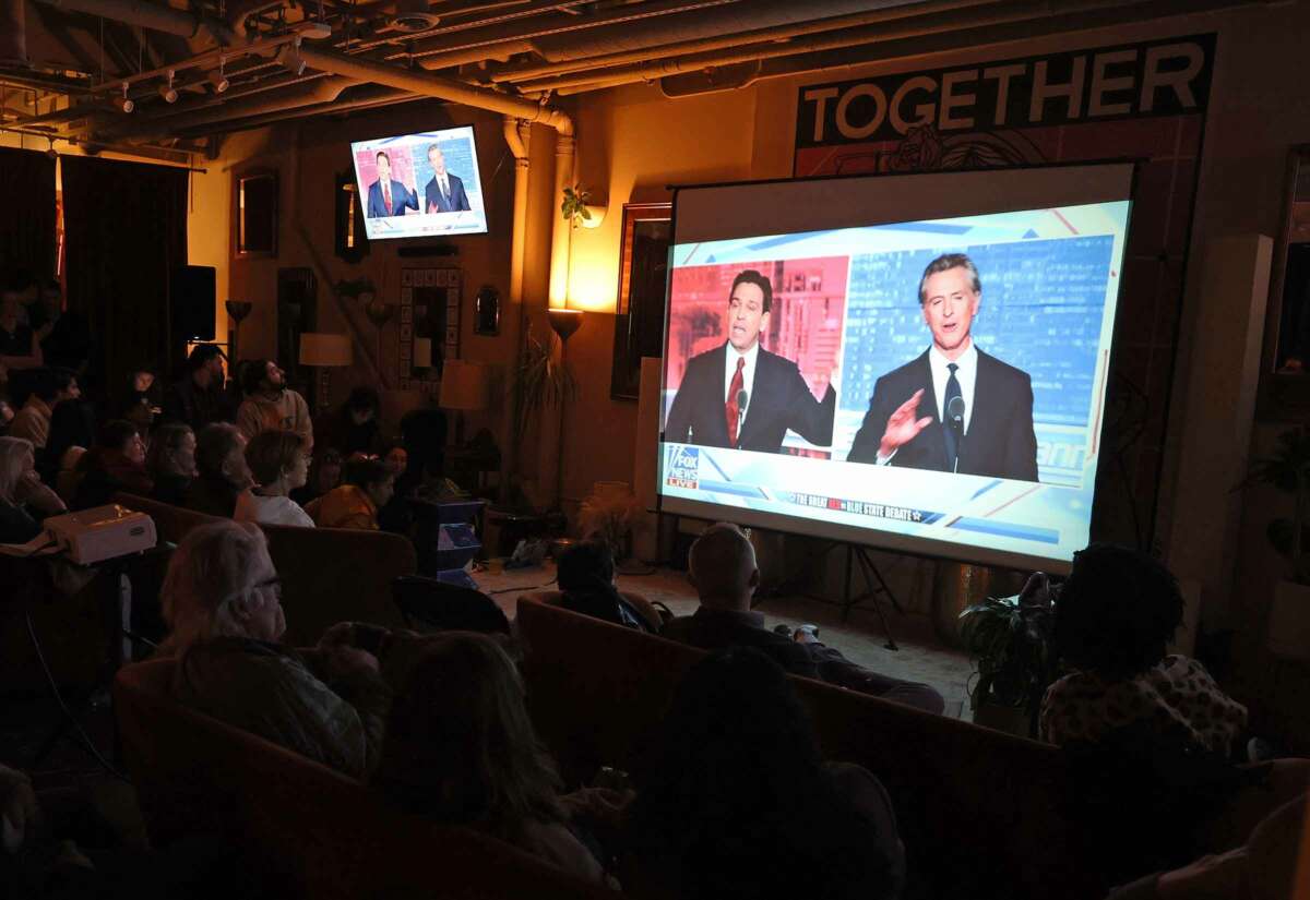 People in a darkened bar watch a televised broadcast of the Gavin Newsom and Ron DeSantis debate