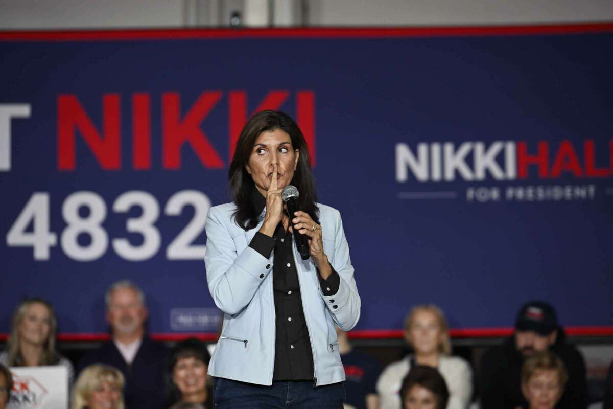 Nikki Haley makes a "shh" gesture by placing her index finger against her lips while speaking into a microphone at a rally