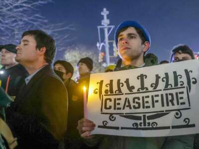 A man holds a sign with an image of a menorah with the word "CEASEFIRE" written across it during an outdoor demonstration