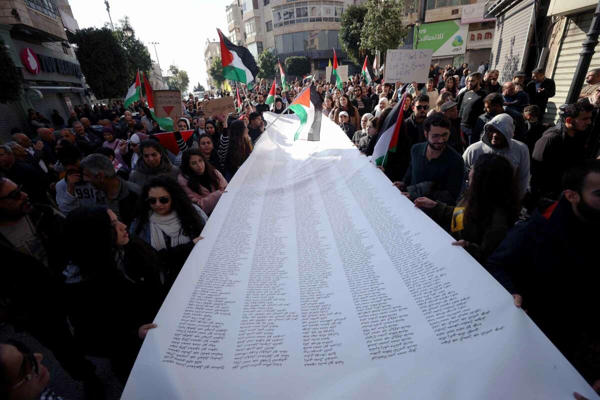 People gathered in a street for a demonstration carry a long list of the names of people martyred during Israeli attacks on Palestine