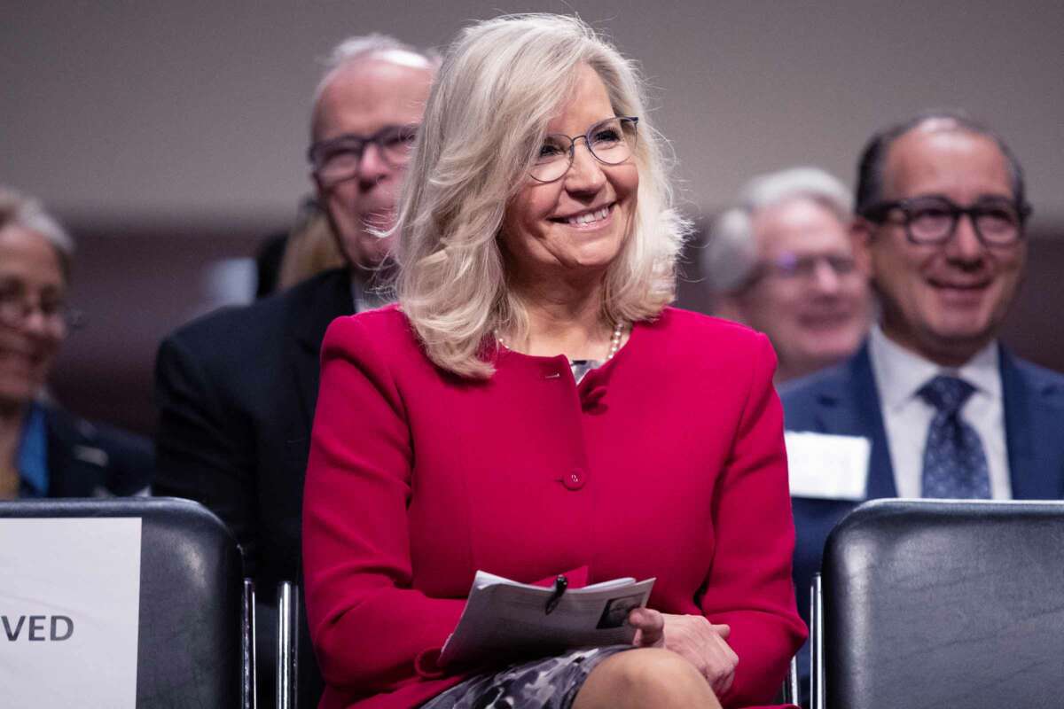 Liz Cheney sits on a chair and smiles