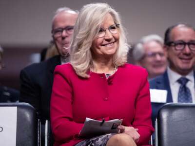 Liz Cheney sits on a chair and smiles