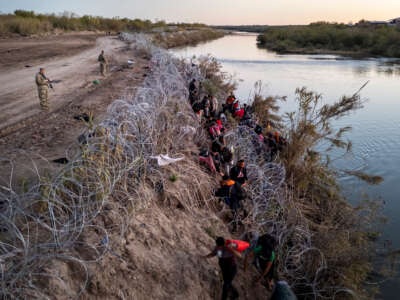 Texas National guardsmen watch as migrants pick their way through razor wire after crossing the Rio Grande into the United States on December 17, 2023, in Eagle Pass, Texas.