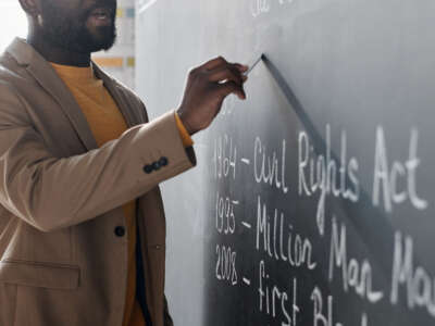 Black teacher writes on chalkboard
