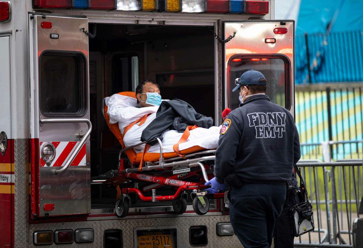 A man on a gurney is wheeled either into or out of an ambulance by paramedics