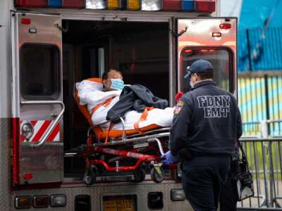 A man on a gurney is wheeled either into or out of an ambulance by paramedics