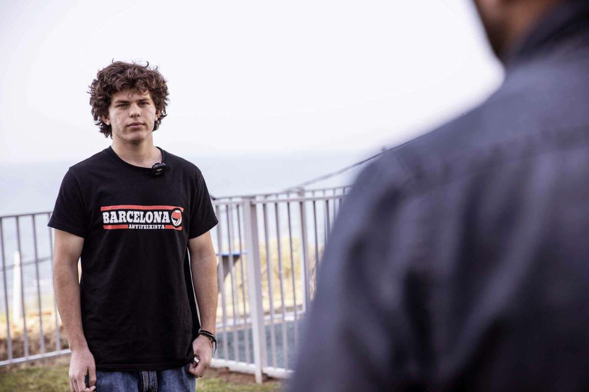 Tal Mitnick stands outside and speaks to someone wearing a blue shirt, whose back is out of focus and facing the camera