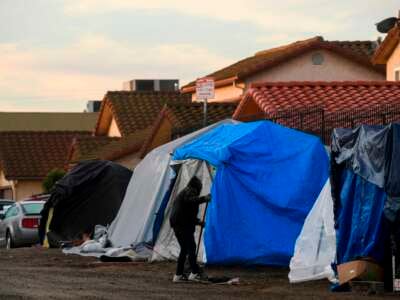 People experiencing homelessness sweep the area around their tent shelters in Los Angeles