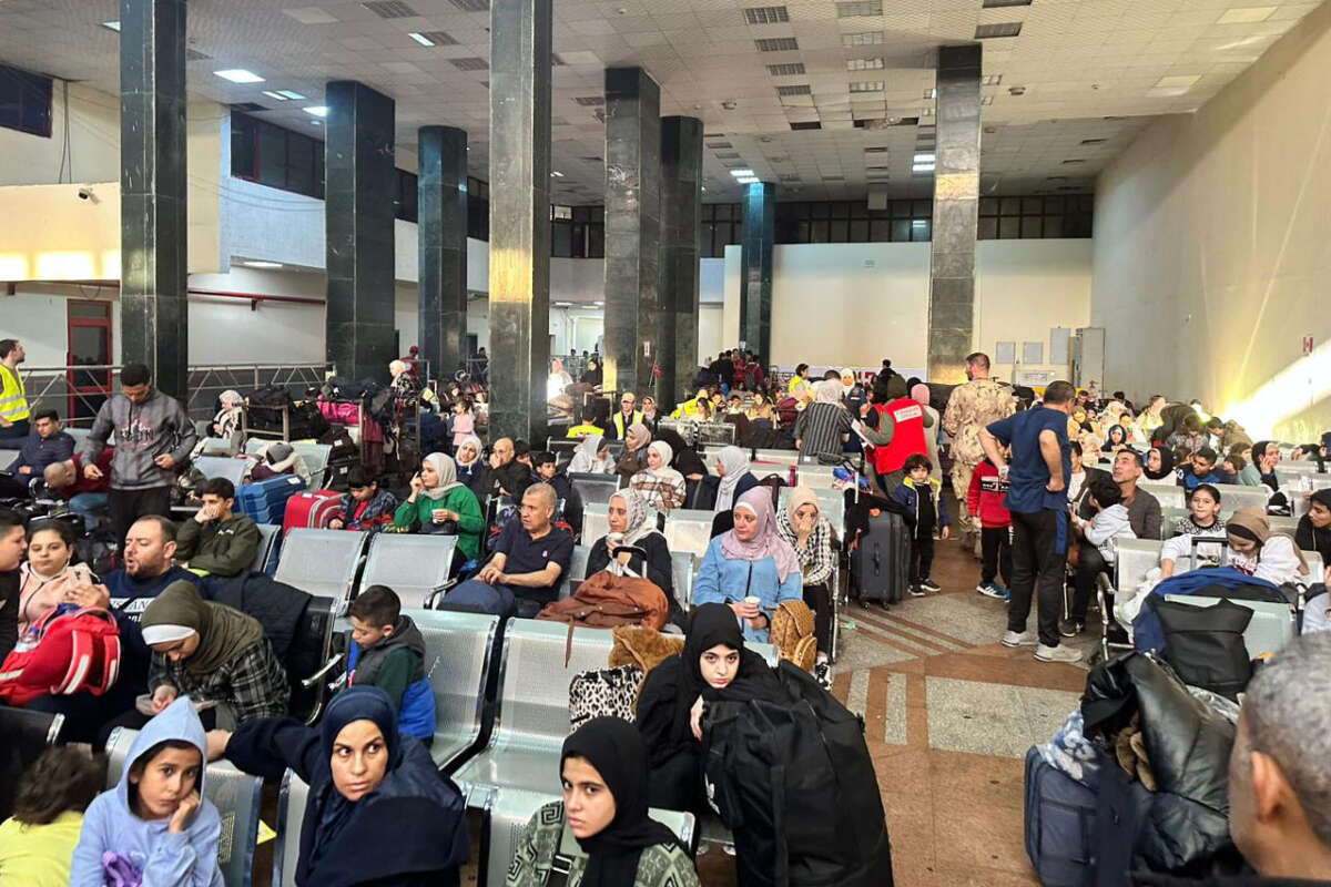 People fleeing from the Gaza Strip wait in a crowded room with suitcases