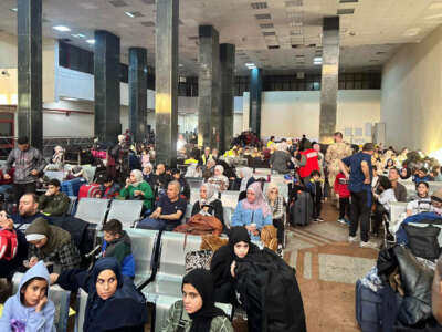 People fleeing from the Gaza Strip wait in a crowded room with suitcases