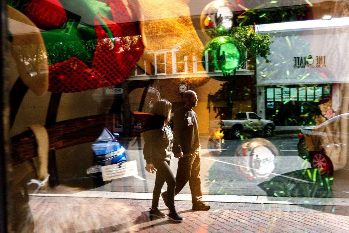 Reflected in a festively decorated shop window, shoppers peruse along State Street in downtown Redlands, California, on November 24, 2023.