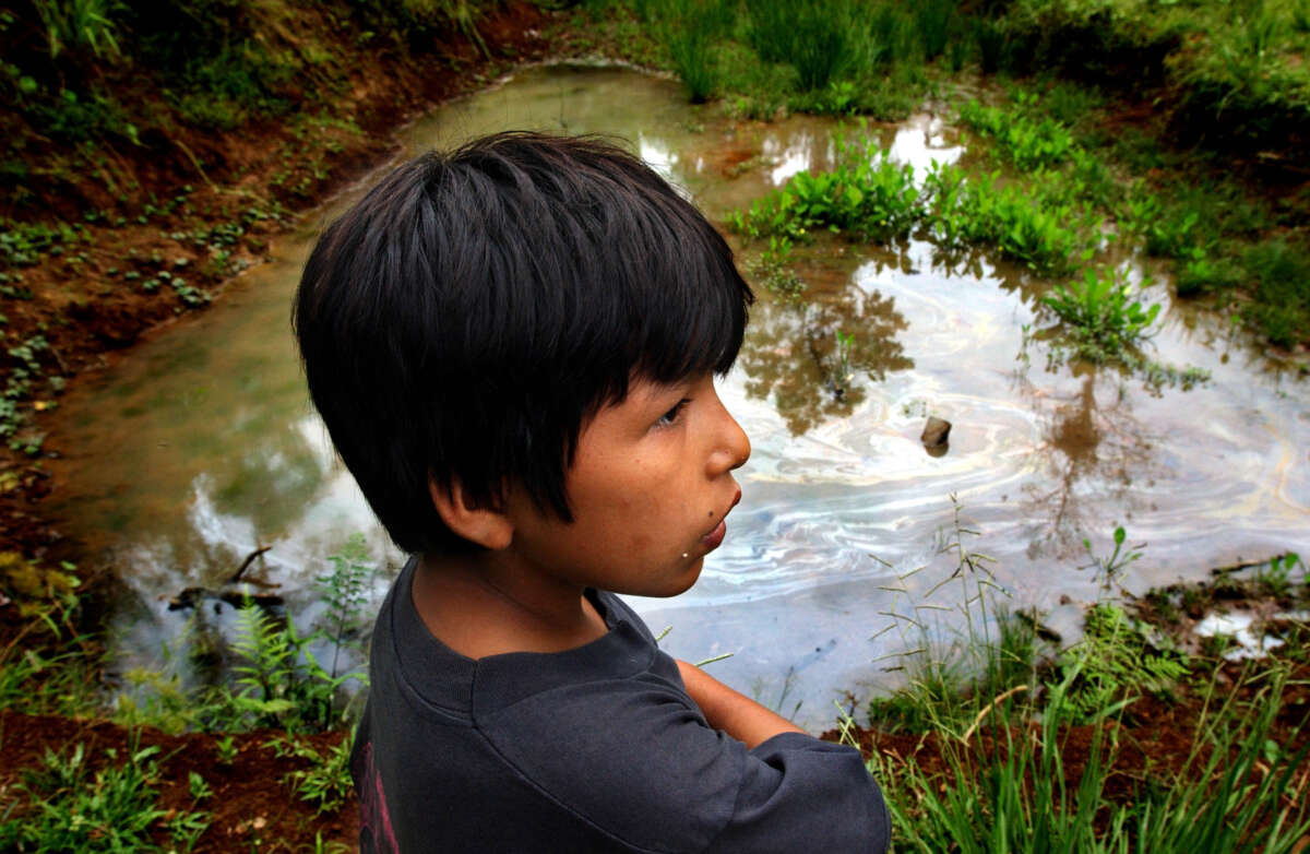 A young boy stands by a pond laced with petroleum residue